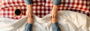Mains entrelacées sur des draps froissés symbolisant l'intimité et la réflexion